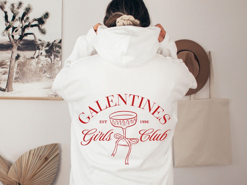 May include: White hoodie with a red graphic print that says "Galentines Girls Club Est 1996" with a stylized image of a champagne glass with a bow.