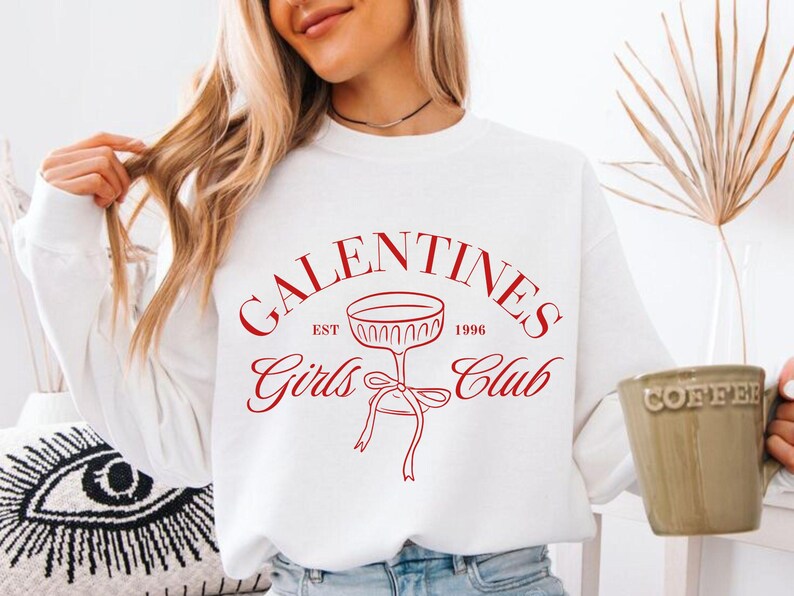 May include: White sweatshirt with red text that reads "Galentines Girls Club Est. 1996" with a red illustration of a champagne glass with a bow.