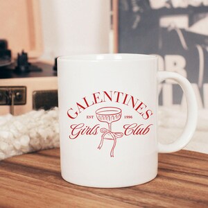 May include: White ceramic mug with a red design that says "Galentines Girls Club Est. 1996" with a stylized glass of champagne.