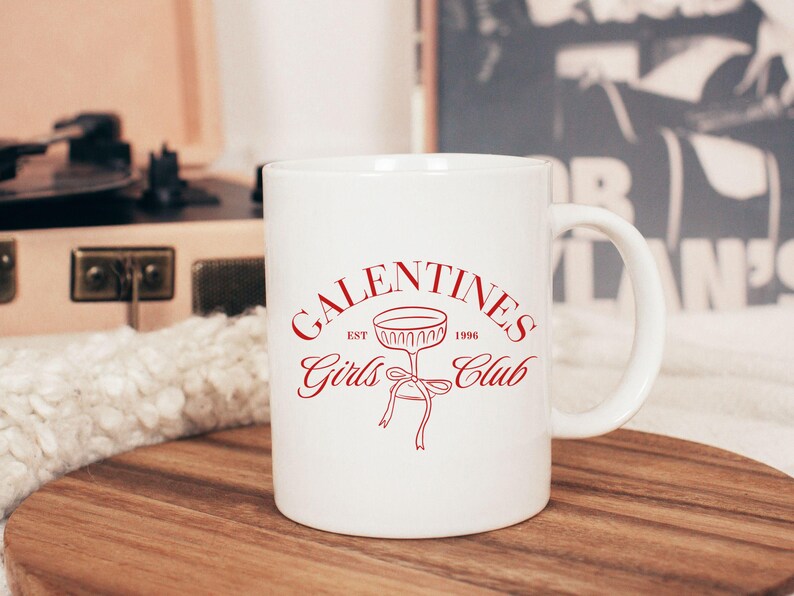 May include: White ceramic mug with a red design that says "Galentines Girls Club Est. 1996" with a stylized glass of champagne.