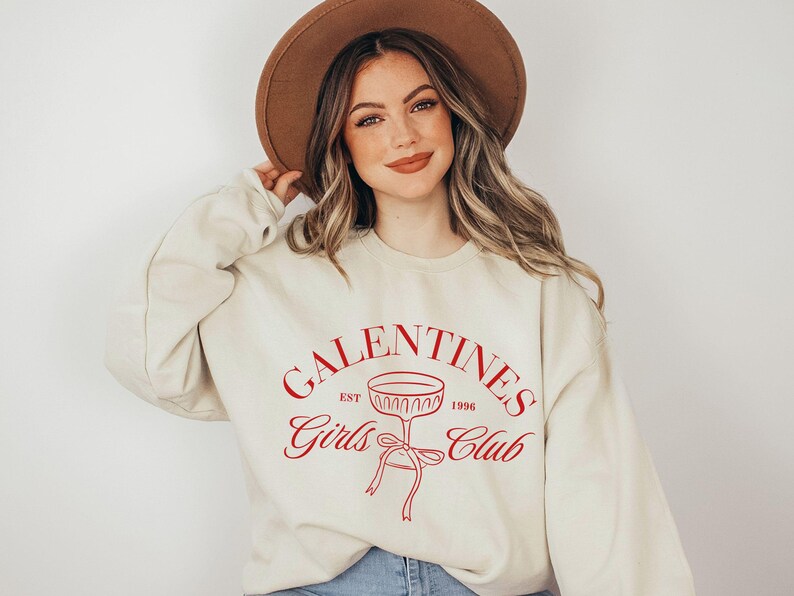 May include: A cream-colored sweatshirt with a red graphic that says "Galentines Girls Club Est. 1996" with a wine glass illustration.