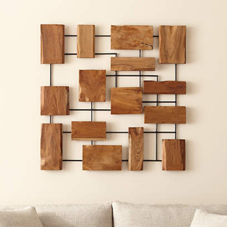 Op de afbeelding: Een wandsculptuur gemaakt van natuurlijke houten stukken die in een geometrisch patroon zijn gerangschikt. De houten stukken zijn bevestigd aan een zwart metalen frame.