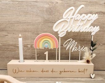 May include: Wooden birthday decoration featuring a rainbow, the number one, a candle holder, and the words "Happy Birthday Marie" and "Wie schön, dass du geboren bist!"