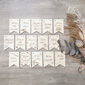 Könnte beinhalten: Ein Set aus 14 Holz-Bannerflaggen mit aufmunternden Sprüchen auf Deutsch, wie "Ich bin stark!" und "Ich bin genug!" Jede Flagge zeigt eine kleine Illustration, wie einen Löwen, einen Regenbogen oder einen Heißluftballon.