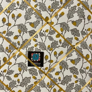 May include: A white cork board with a gold ribbon grid pattern. The board is covered in a fabric with a grey and yellow acorn and leaf pattern. The text "Lisa Peter" and "Pottery Rose" is visible in the lower right corner.