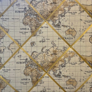 May include: A corkboard with a world map printed on it. The corkboard is divided into sections by gold-colored ribbons that are attached with gold-colored tacks. The map is in a vintage style with brown and beige colors.