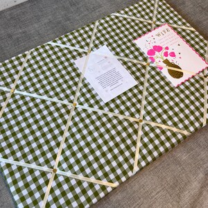 May include: A green and white gingham fabric memo board with cream-colored ribbons and gold-colored tacks. A greeting card that says "Wife" and a small white card are attached to the board.