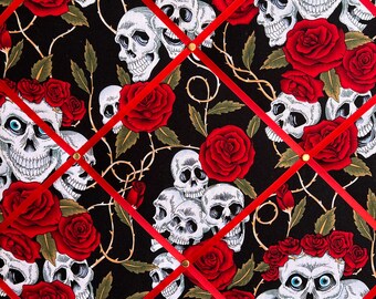 May include: A black fabric bulletin board with red ribbon crisscrossing the surface. The fabric features a repeating pattern of white skulls and red roses. The board has a business card attached to it with the text "www.prettystone.co.uk".