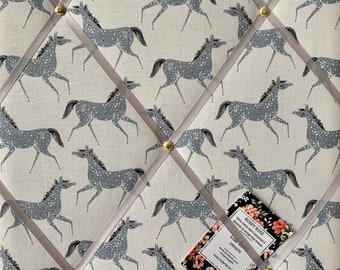 May include: A white fabric notice board with a gray horse pattern. The board is decorated with gray satin ribbon and gold push pins. A business card for "Rosy Rose" is pinned to the board.