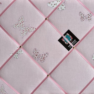 May include: A pink fabric notice board with a diamond pattern of pink ribbon. The board is decorated with white butterflies with pink floral patterns. A business card is pinned to the board.