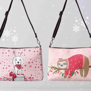 May include: Two pink crossbody bags with black straps. One bag features a white dog wearing a red bandana and antlers, sitting on a gift box. The other bag shows a sloth wearing a red sweater, resting on a branch with Christmas lights.