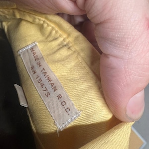 May include: Close-up of a yellow garment with a tag that reads "MADE IN TAIWAN R.O.C." and "RN 15475". The fabric is a light yellow color and appears to be cotton or a similar material. The garment is being held by a hand.
