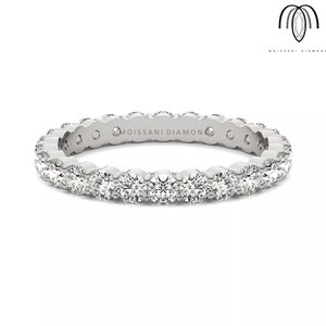 以下が含まれることがあります： 丸い透明な輝く石が並んだシルバーの永遠のバンド。バンドには「モアサナイトダイヤモンド」という文字が刻まれています。