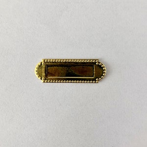 May include: A gold-coloured metal nameplate with a beaded border. The nameplate is blank and ready to be engraved.