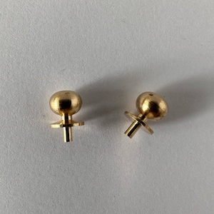 May include: Two small, gold-coloured metal ball finials with a post and a small, round base. The finials are on a white surface. The ball is at the top of the finial.