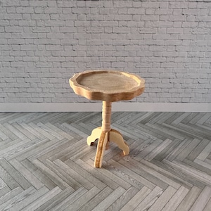 May include: A miniature wooden side table with a scalloped edge tabletop. The table has a pedestal base with three curved legs. The wood has a natural, unfinished appearance. The table is designed for a dollhouse or miniature setting.