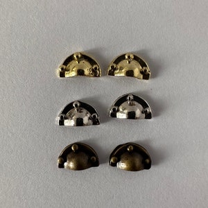 May include: Six small metal drawer pulls in three different finishes: gold, silver, and antique brass. Each pull is shaped like a half-circle with a rounded top and three decorative knobs.