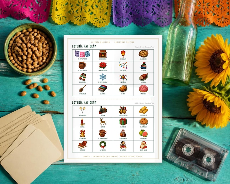 May include: A white Loteria Navide&ntilde;a game board featuring two grids of colourful Christmas-themed illustrations and Spanish text labels. The board is surrounded by a bowl of beans, a stack of blank cards, a glass bottle, sunflowers, and a cassette tape.