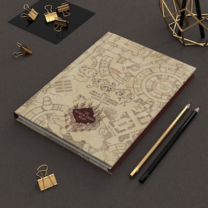 May include: A brown leather-bound journal with a marauder's map design. The map features a detailed illustration of Hogwarts castle and surrounding grounds. The text "The Marauder's Map" is printed in black on the cover.