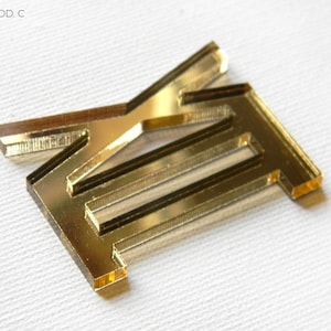 Op de afbeelding: Goudkleurige acryl letter "E" en een deel van de letter "A" op een witte ondergrond. De letters zijn van de collectie "ROMA MOD. C". De afbeelding bevat ook het "Glow Me" logo en de tekst "MADE IN ITALY".
