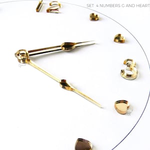 May include: A close-up of a clock face with gold hands and numerals. The numbers 1, 2, and 3 are visible, along with heart-shaped markers. The text "SET 4 NUMBERS G AND HEARTS DASHES" is at the top.