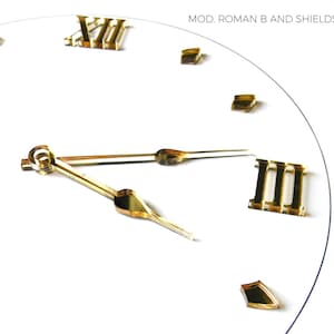 May include: A white clock face with gold Roman numerals and hands. The clock hands point to approximately 2:10. The text "MOD. ROMAN B AND SHIELDS DASHES" is at the top. The clock is made in Italy.