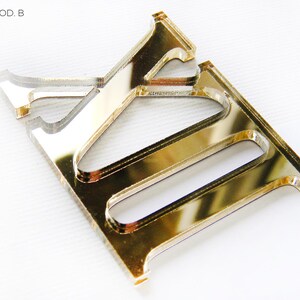 May include: A gold-colored acrylic letter "E" with a reflective surface. The letter is part of the "ROMA MOD. B" series. The image also includes the "Glow Me" logo and "MADE IN ITALY" text.