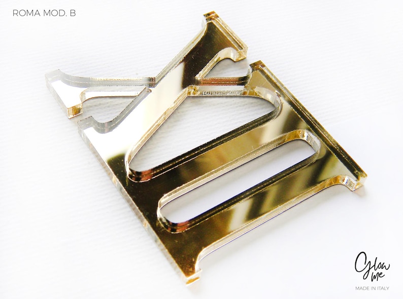 May include: A gold-colored acrylic letter "E" with a reflective surface. The letter is part of the "ROMA MOD. B" series. The image also includes the "Glow Me" logo and "MADE IN ITALY" text.