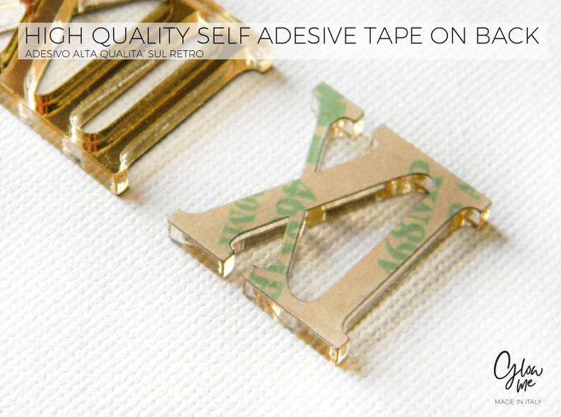 May include: Close-up of gold-colored metal letter cutouts with adhesive tape on the back. The letters are on a white textured surface. Text at the top reads "HIGH QUALITY SELF ADHESIVE TAPE ON BACK". The bottom right corner has the text "Glow Me MADE IN ITALY".