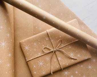 May include: A roll of brown kraft wrapping paper featuring a repeating white starburst pattern, alongside a rectangular gift box wrapped in the same paper and tied with a thin, natural-colored jute twine bow.