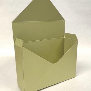 May include: A light olive green metal container shaped like an open envelope. The box features a triangular flap at the top and a rectangular base, with a smooth, matte finish and clean, sharp edges throughout the entire structure.