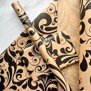 May include: A collection of wrapping paper sheets and a roll featuring a tan background with a repeating black ink swirl and teardrop pattern. The paper displays a consistent graphic design across the flat sheets and the cylindrical roll.
