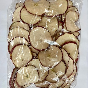 Może przedstawiać: Przezroczysta plastikowa torba wypełniona suszonymi plasterkami jabłek. Plasterki jabłek są okrągłe, z jasno-beżowym środkiem i czerwonobrązową krawędzią. Torba jest zamknięta, a zawartość widoczna.