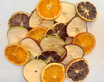 May include: A collection of dehydrated fruit slices including bright orange citrus rounds, pale green apple rings, and dark brown dried citrus segments. The assorted pieces are arranged in a cluster, showcasing varied textures and natural colors.