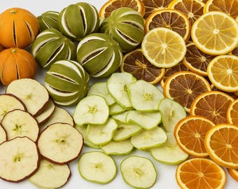 May include: A collection of dried fruit including whole oranges and limes with vertical slits, alongside thin, circular slices of apples, lemons, and oranges. The assortment features vibrant shades of orange, lime green, and pale yellow throughout.