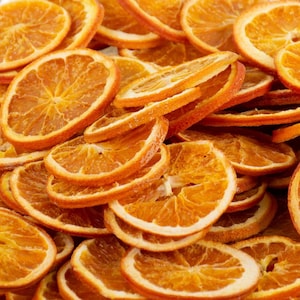 Puede incluir: Primer plano de rodajas de naranja deshidratadas, mostrando un color naranja vibrante y una superficie texturizada. Las rodajas están apiladas, algunas superpuestas. La imagen resalta los patrones y texturas naturales de la fruta deshidratada, ideal para manualidades o decoración.
