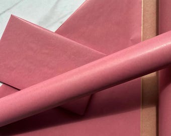 May include: A roll and flat sheets of solid dusty rose pink wrapping paper. The paper features a subtle, fine-lined vertical texture throughout its surface, providing a matte finish to the material used for gift packaging and craft projects.