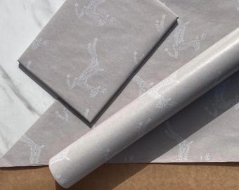 May include: Light gray wrapping paper featuring a repeating white line art pattern of rabbits surrounded by floral elements. The paper is presented as both a flat rectangular sheet and a tightly rolled cylinder of the same material.