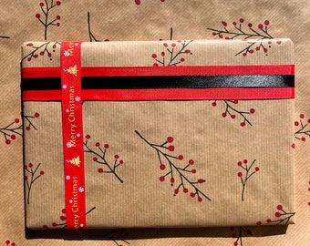 May include: A wrapped gift on brown paper with a red berry branch pattern. The gift is secured with a red and black ribbon, and a red ribbon with "Merry Christmas" text. The wrapping paper is also decorated with red berry branches.