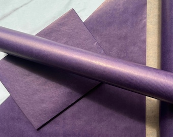 May include: A roll of deep purple wrapping paper with a subtle, fine-lined texture. The paper is partially unrolled, revealing a smooth, matte finish on the exterior and a lighter, neutral-toned interior side of the paper sheet.
