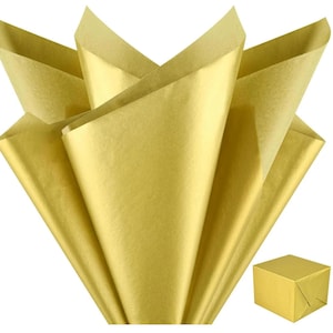 Può includere: Carta velina dorata a ventaglio, con una piccola scatola dorata avvolta nell'angolo. La carta velina è piegata a forma di ventaglio, con i bordi dei fogli visibili. La scatola è quadrata e avvolta nella stessa carta dorata.