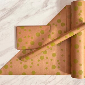 Op de afbeelding: Bruin kraftpapier cadeaupapier met een patroon van lichtgroene stippen. De afbeelding toont een verpakt pakket, een vel en een rol papier. Het papier heeft een warme bruine kleur en is versierd met hetzelfde ontwerp.