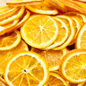 Könnte beinhalten: Eine Ansammlung getrockneter Orangenscheiben, die jeweils einen leuchtend gold-orangen Farbton mit einer durchscheinenden, faserigen Fruchtfleischstruktur und einer ausgeprägten, dünnen weißen Schale aufweisen. Die runden Fruchtsegmente sind geschichtet.