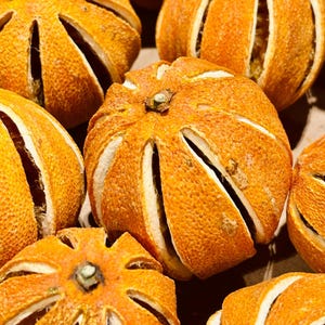 Puede incluir: Primer plano de varias rodajas de naranja secas, cada una con un patrón en forma de estrella cortado en la cáscara. Las naranjas son de un color naranja vibrante, con una superficie texturizada. Las secciones cortadas revelan el interior blanco de la fruta.