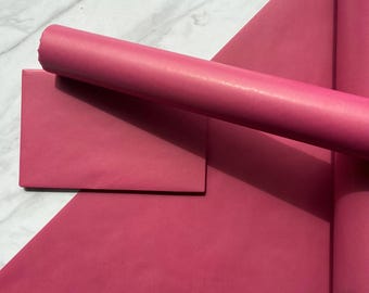May include: A roll of solid dark pink paper positioned next to a flat, rectangular sheet of the same dark pink paper. The paper has a smooth, matte texture and a consistent, vibrant magenta-pink color throughout the entire surface area.