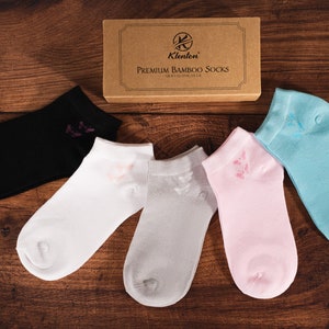 May include: Five pairs of ankle socks in different colours: black, white, grey, pink, and light blue. Each sock has a small butterfly design on the top.