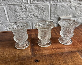 May include: Three clear glass bud vases with a diamond pattern. The vases have a round base and a flared top.
