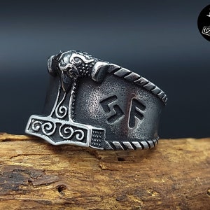 Può includere: Un anello d'argento con un designo dettagliato di un martello e rune. L'anello è realizzato in acciaio inossidabile e ha una finitura testurizzata.