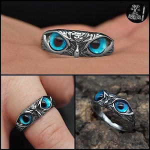 Può includere: Un anello argentato con un design a gufo e occhi blu brillante. L'anello presenta dettagli intricati attorno agli occhi e alla testa, creando un gioiello unico. L'anello è mostrato da più angolazioni.