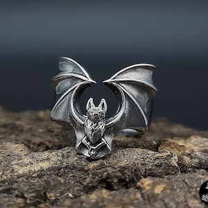 Op de afbeelding: Een zilveren ring met een gedetailleerd vleermuisontwerp. De vleermuis heeft uitgespreide vleugels en zit op een ringband.